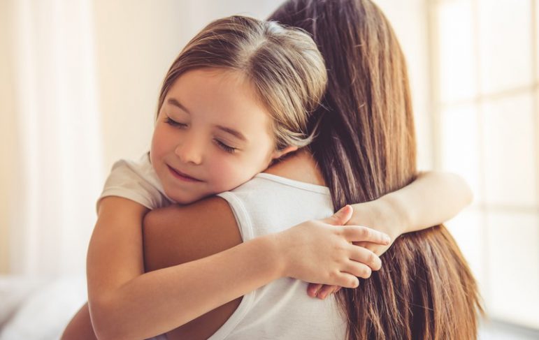 Beautiful young woman and her charming little daughter are hugging and smiling