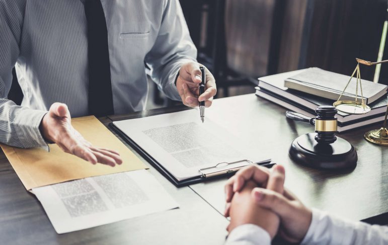 A lawyer and a client engaged in discussion at a desk, reviewing legal documents together in a professional setting.
