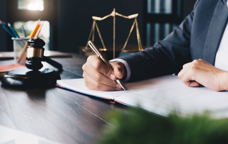 A focused lawyer using a pen to write on paper, with the scales of justice prominently displayed nearby.