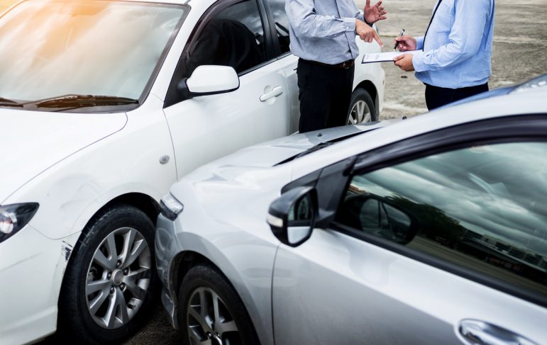 Insurance agent writing on clipboard while examining car after a